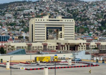 Edificio del Congreso Nacional de Chile, una construcción clara de gran altura con un arco central, frente a los cerros poblados de casas de colores de Valparaíso.