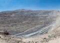 Vista panorámica de un enorme rajo abierto con bancos escalonados grises en el desierto, bajo un cielo azul despejado.