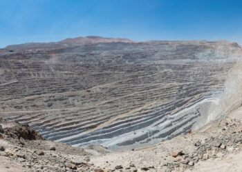 Vista panorámica de un enorme rajo abierto con bancos escalonados grises en el desierto, bajo un cielo azul despejado.