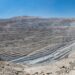 Vista panorámica de un enorme rajo abierto con bancos escalonados grises en el desierto, bajo un cielo azul despejado.