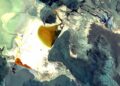 Imagen satelital de un salar blanco con pozas de evaporación de tonos ocres y naranjas, rodeado de montañas oscuras.