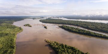 Vista aérea del río Xingu, de aguas color café, con islas cubiertas de selva amazónica y bosque denso en ambas orillas bajo un cielo parcialmente nublado.