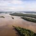 Vista aérea del río Xingu, de aguas color café, con islas cubiertas de selva amazónica y bosque denso en ambas orillas bajo un cielo parcialmente nublado.