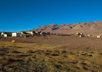 Pequeño poblado de casas bajas en la Puna salteña, con un terreno de pasto seco en primer plano y cerros áridos de tonos ocres bajo un cielo azul despejado.