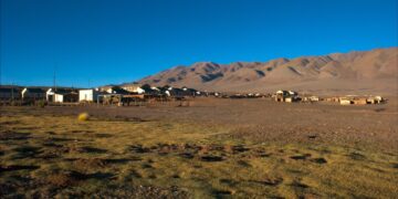 Pequeño poblado de casas bajas en la Puna salteña, con un terreno de pasto seco en primer plano y cerros áridos de tonos ocres bajo un cielo azul despejado.