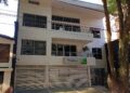 Fachada de un edificio blanco de tres pisos con el letrero verde de la Agencia Nacional de Minería sobre la entrada, junto a un árbol, en una calle de Medellín.